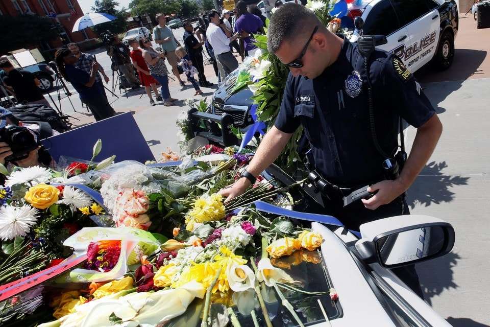 A Dallas police officer observes a moment of silence after putting some flowers on a police car that makes up part of a makeshift memorial at Police Headquarters following the multiple police shooting in Dallas, Texas, U.S.,July 8, 2016. REUTERS/Carlo Allegri